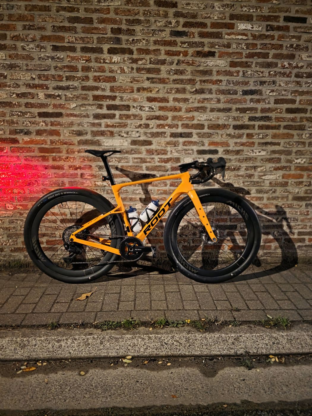 Oranje ROOT aero gravelfiets tegen een bakstenen muur